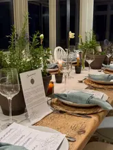 A beautifully styled, atmospheric shot of a supper club table setting, featuring elegant place settings, candles, and fresh herbs, capturing an intimate and curated dining experience.