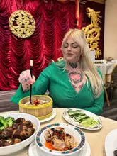 A portrait-style shot of a diner enjoying a spread of Chinese dishes at a restaurant. The image captures the authentic atmosphere of the venue with traditional decor in the background, while the foreground features a variety of dishes, creating an inviting and social dining scene.
