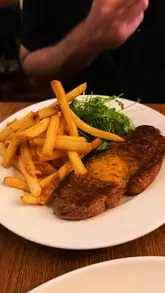 A review of the restaurant Marcel in Belfast, showcasing their new location on Lisburn Road. The video features close-up shots of various dishes including steak frites, baked camembert, chicken with mushroom sauce, and dessert, alongside glimpses of the restaurant's interior and exterior.