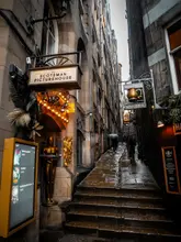 A moody, atmospheric, and high-quality photograph of Fleshmarket Close in Edinburgh, capturing the historic, narrow alleyway with signage for The Scotsman Picturehouse and The Halfway House. The image effectively conveys the unique, dark, and historic charm of the location.