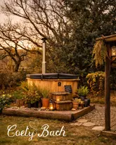 A beautifully composed, atmospheric shot of a wood-fired hot tub in a rustic, natural setting, perfectly capturing the 'slow living' and romantic escape vibe of the venue.