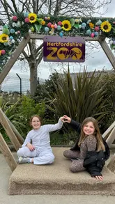 A montage video featuring two young girls visiting Hertfordshire Zoo, showcasing various animals including monkeys, meerkats, a wallaby, a zebra, and alpacas, as well as photo opportunities around the park.
