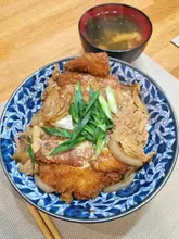 A top-down shot of a homemade tonkatsu-don bowl served with a side of miso soup, captured on a wooden table.
