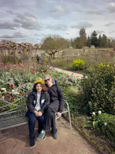A casual, candid family snapshot taken at a National Trust estate during an Easter activity trail. The subjects are seated on a metal bench in a garden setting.