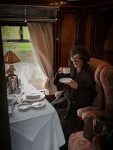 A high-quality, atmospheric shot of a passenger enjoying tea aboard the Belmond British Pullman luxury train, showcasing the vintage interior and elegant table setting.