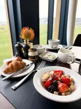 A high-quality, well-composed shot of a hotel breakfast spread featuring a croissant, a bowl of fruit and granola, and various condiments, set against a scenic window view of a golf course.