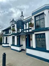 A clear, eye-level exterior shot of The Horse and Farrier pub in Gatley, capturing the building's traditional facade, signage, and hanging baskets under an overcast sky.