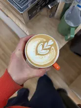 A top-down, first-person perspective shot of a freshly poured latte featuring tulip-style latte art, held by a barista in a cafe environment.