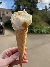 A handheld shot of a scoop of clotted cream and honeycomb ice cream in a waffle cone, taken outdoors on a sunny day at Lotherton Hall.
