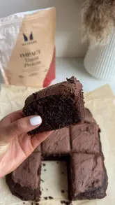 A short-form recipe tutorial demonstrating how to bake a vegan protein chocolate cake. The video features top-down shots of the mixing process and handheld shots of the creator presenting and tasting the finished cake.