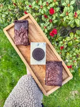 A top-down shot of a wooden tray holding two chocolate brownies and a square of Oreo-topped fudge, held by a person wearing a fleece sleeve against a background of garden foliage.