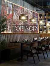 A professionally captured interior shot of the restaurant Tori Nori, highlighting its sophisticated and warm ambiance. The image features elegant booth seating, stylish pendant lighting, and detailed wall art, creating an inviting atmosphere for diners.