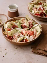 A high-quality, professionally styled food photograph featuring a vibrant salmon and citrus salad. The image uses soft, natural lighting and a neutral, textured background to highlight the fresh ingredients, including blood orange, fennel, and avocado. The composition is clean and inviting, clearly showcasing the texture and colours of the dish.