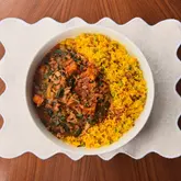 A top-down, well-composed photograph of a homemade paneer curry served alongside vibrant yellow pea rice in a white bowl, set on a scalloped placemat on a wooden surface.