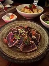A moody, well-composed close-up shot of tuna tataki, highlighting the fresh texture of the fish and the restaurant's intimate, low-light atmosphere.