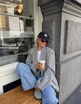 A lifestyle-focused shot of a person sitting on an outdoor bench outside a cafe, holding an iced coffee. The image captures a relaxed, sunny spring atmosphere, typical of social media content promoting a casual coffee spot.