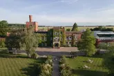 An aerial drone shot of a large, ivy-covered brick country house hotel set in extensive grounds, showcasing the scale and setting of the venue.