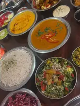 An overhead flat-lay shot of a table spread featuring a variety of Indian dishes served in metal bowls, including curries, rice, and side salads.