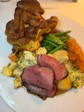 A standard, unpretentious Sunday roast featuring beef, a large Yorkshire pudding, and a selection of vegetables, presented on a plain white plate.