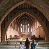A wide-angle, symmetrical shot taken from behind three children looking into the grand, brick-arched interior of Quarr Abbey on the Isle of Wight. The image captures the scale and architectural beauty of the space, using the children as a focal point to draw the viewer's eye into the depth of the building.