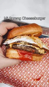 A short, energetic reel showcasing a limited-edition 'Mi Goreng Cheeseburger' collaboration at Zula Burger in Marylebone. The video features close-up shots of the burger, the preparation process in the kitchen, and the accompanying fries and sauces.