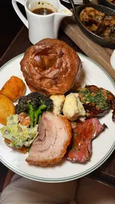 A review of a Sunday Roast at The George in London, featuring a sharer board with beef, pork, and lamb, accompanied by bone marrow gravy and crispy roast potatoes. The video also highlights starters like fried chicken and dessert, set against the backdrop of live Irish music.