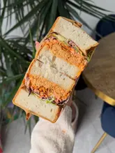 A high-quality, close-up shot of a sandwich held in a hand, effectively showcasing the cross-section and layers of ingredients. The lighting is soft and natural, highlighting the textures of the bread, meat, and slaw, while the shallow depth of field keeps the focus entirely on the food.