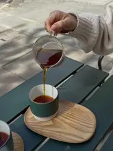 A high-quality, aesthetic shot of a pour-over coffee being served at a cafe, focusing on the action of the pour into a stylish green cup on a wooden tray.