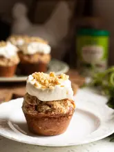 A high-quality, visually appealing image of a carrot cake cupcake topped with cream cheese frosting and chopped pecans, set on a white plate. The image is clean, well-lit, and professionally composed, though it exhibits characteristics typical of AI-generated imagery.