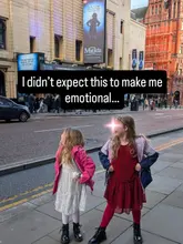 A candid shot of two young girls posing on a city sidewalk in front of the Palace Theatre in Manchester, capturing a family outing to see a musical.