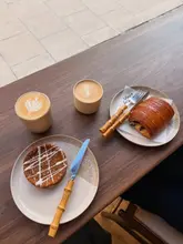 A high-quality, aesthetically pleasing flat-lay shot of a cafe table featuring two coffees, a pastry, and a small tart, set against a clean wooden surface.