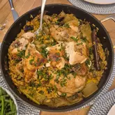 A top-down shot of a one-pot chicken and orzo dish served in a pan, featuring celery and mushrooms, presented on a dining table.