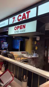 A short, rhythmic video showcasing '7th Cat', a late-night Cantonese restaurant in London. The video features quick cuts of the restaurant interior, the kitchen staff preparing food, and close-ups of various dishes including roast duck, wonton, and salt and pepper squid, set to music with text overlays detailing the menu items.