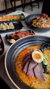 A montage video showcasing the interior, food, and drinks at a Maki & Ramen restaurant. The video features shots of ramen, small plates, cocktails, and mochi, alongside the restaurant's signature cherry blossom decor and a wall covered in customer notes.