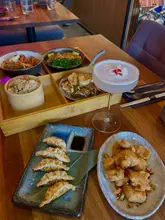 A top-down and angled shot of a table spread at Man Zen, featuring a bento box, various small plates, and a cocktail. The image captures a 'feast' style dining experience with multiple dishes arranged on the table.