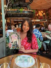 A bright, well-composed portrait of a creator holding the 'Taste of Spring' menu at The Ivy, effectively showcasing the restaurant's interior and branding.
