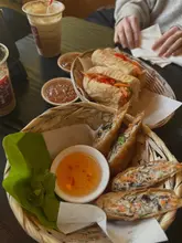 A high-angle, natural-light shot of Vietnamese street food, including summer rolls and a chicken banh mi, served in woven baskets on a dark table.