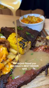 A promotional video for a smokehouse restaurant in Blackburn, featuring close-up shots of a large meat platter, a double-patty burger, chicken tenders, mocktails, and dessert. The video uses a voiceover to describe the food and includes text overlays to highlight key dishes and the venue's location.