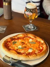 A straightforward, well-lit shot of a Margherita pizza and a pint of Cruzcampo beer on a pub table, effectively capturing a classic casual dining moment.