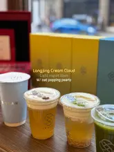 A clean, well-lit product shot of three tea-based drinks from a London tea shop, featuring clear branding and a shallow depth of field to highlight the texture of the drinks.