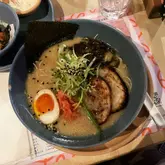 A top-down, slightly angled shot of a bowl of ramen featuring pork chashu, a soft-boiled egg, and green onions, served at a restaurant.