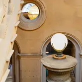 A high-quality architectural shot of the interior of The Hobson Cambridge, showcasing the historic building's features, specifically a spiral staircase and a decorative lamp. The image captures the sophisticated, warm atmosphere of the hotel and its bar area, Oz & Isle.