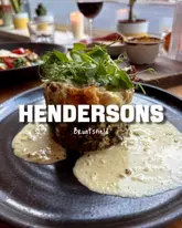 A shot of a plated vegetarian dish, likely a haggis stack, served at Hendersons in Edinburgh. The image features a prominent text overlay identifying the venue.