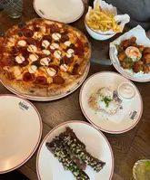 A top-down food spread featuring a pepperoni pizza, fries, ribs, and other small plates at Caffe Rojano.