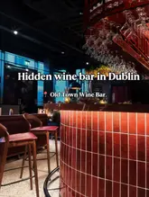 A high-quality, atmospheric interior shot of a wine bar, focusing on the illuminated bar counter and the hanging glassware above. The warm lighting and composition effectively convey a cozy, upscale vibe suitable for an evening out.