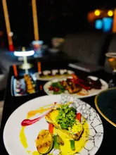 A close-up, eye-level shot of a pan-seared halibut dish served in a dimly lit restaurant, with other dishes visible in the blurred background.