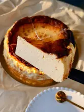 A high-quality, close-up shot of a slice of burnt basque cheesecake being held up by a spatula, effectively showcasing the creamy, soft interior texture against a warm, golden-hour background.