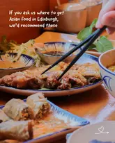 A high-quality, appetizing POV shot of a meal, likely Korean or Japanese fried chicken, being picked up with chopsticks. The lighting is warm and inviting, typical of a restaurant setting, and the focus is sharp on the food, making it highly engaging for social media.