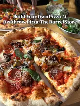A close-up, appetizing shot of a custom-built pizza at a restaurant, with a table spread including salads and drinks, capturing a casual dining experience.
