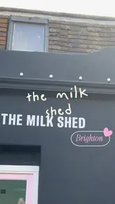 A short, engaging vlog-style video showcasing The Milk Shed in Brighton. The video features exterior shots of the cafe, a look at the interior, and close-ups of their signature cookies and specialty drinks, including a yuzu lemonade, tiramisu latte, and strawberry matcha.